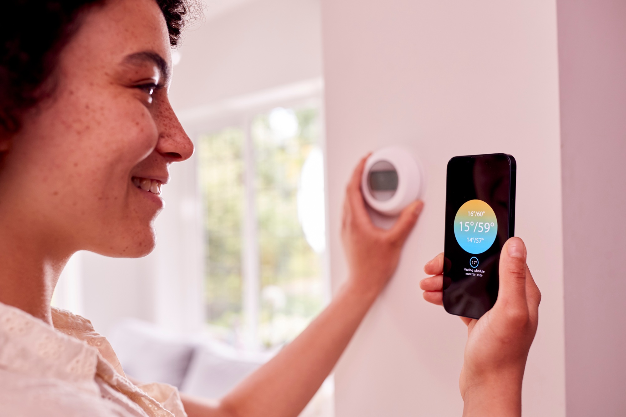 Close Up Of Woman Using App On Mobile Phone To Control Central Heating Thermostat At Home